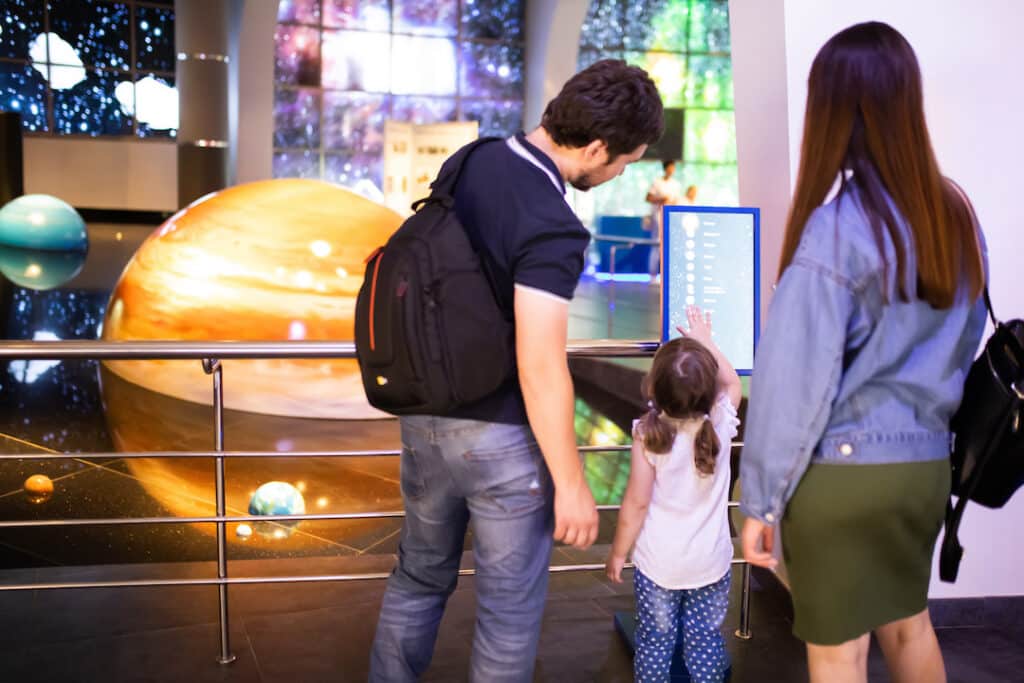 Das Bild zeigt eine junge Familie an einem Touchscreen in einer Ausstellung